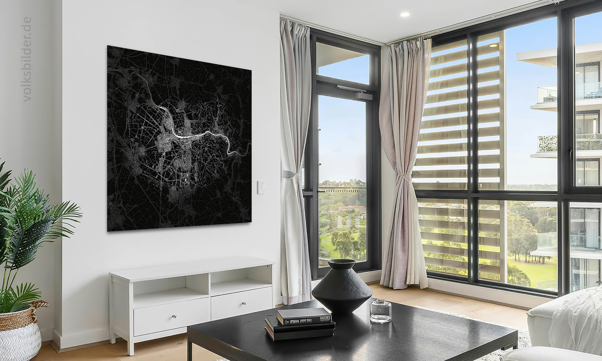 Das Foto zeigt ein Wohnzimmer in einem Hochhaus. Rechts sieht man durch ein großes Fenster ein weiteres Hochhaus. Links an einer Wand im Hintergrund hängt ein schwarz-weißes Bild mit der Landkarte von Heidelberg und Umgebung.