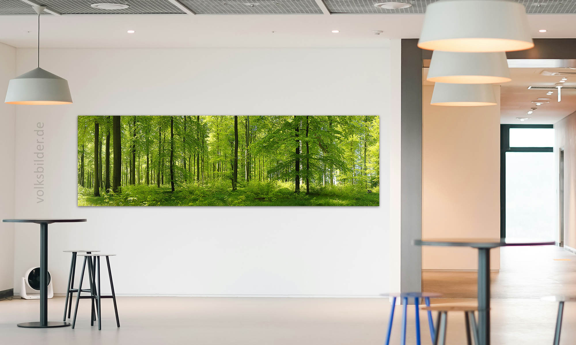 Das Foto zeigt eine Veranstaltungshalle mit Stehtischen und Barhockern. An der Wand im Hintergrund hängt ein langes, großes Panorama-Wandbild. Es zeigt einen Buchenwald im Frühjahr mit alten und jungen Bäumen. Das Laub der Bäume ist leuchtend hellgrün. Der Waldboden ist mit Seegras bedeckt.