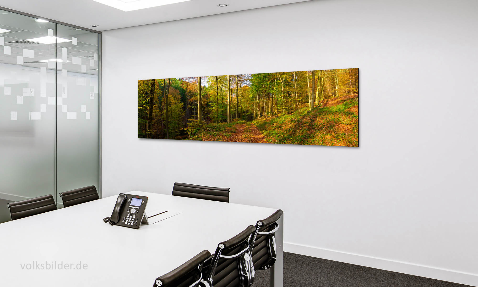 Das Foto zeigt ein Besprechungszimmer oder einen Konferenzraum in einer Firma oder in einem Büro. Im Raum stehen ein großer Tisch und mehrere Stühle. Auf dem Tisch steht ein Telefon. An der Wand im Hintergrund hängt ein langes, großes Panorama-Wandbild. Es zeigt den herbstlich bunten Wald bei Edenkoben in Rheinland-Pfalz.